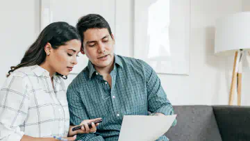 A couple sits on a couch reading a piece of paper